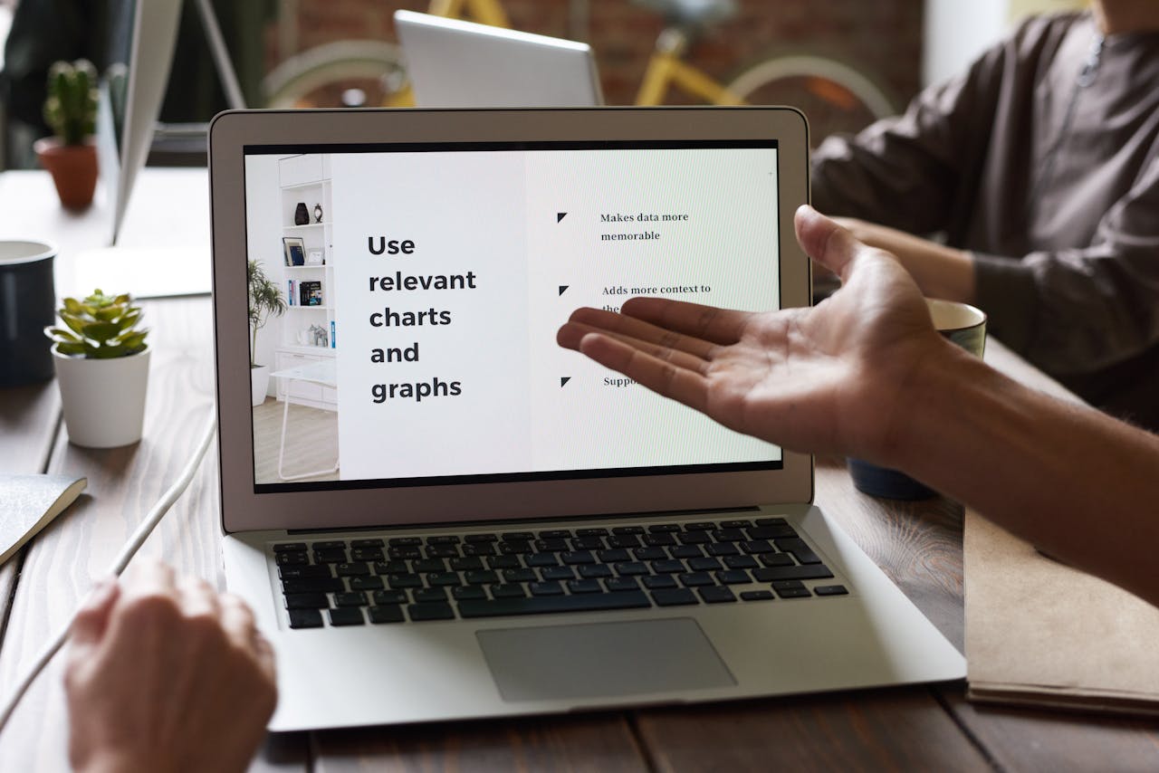 Close-up of a business meeting with hands gesturing toward a laptop screen.